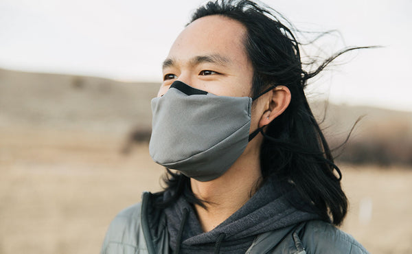 Person standing outdoors in a grassy field wearing the V6 Mask in True Grey.